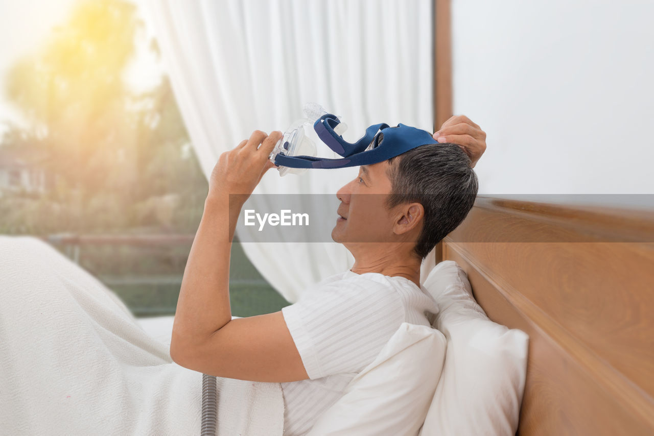 Side view of patient wearing oxygen mask while sitting on bed in hospital