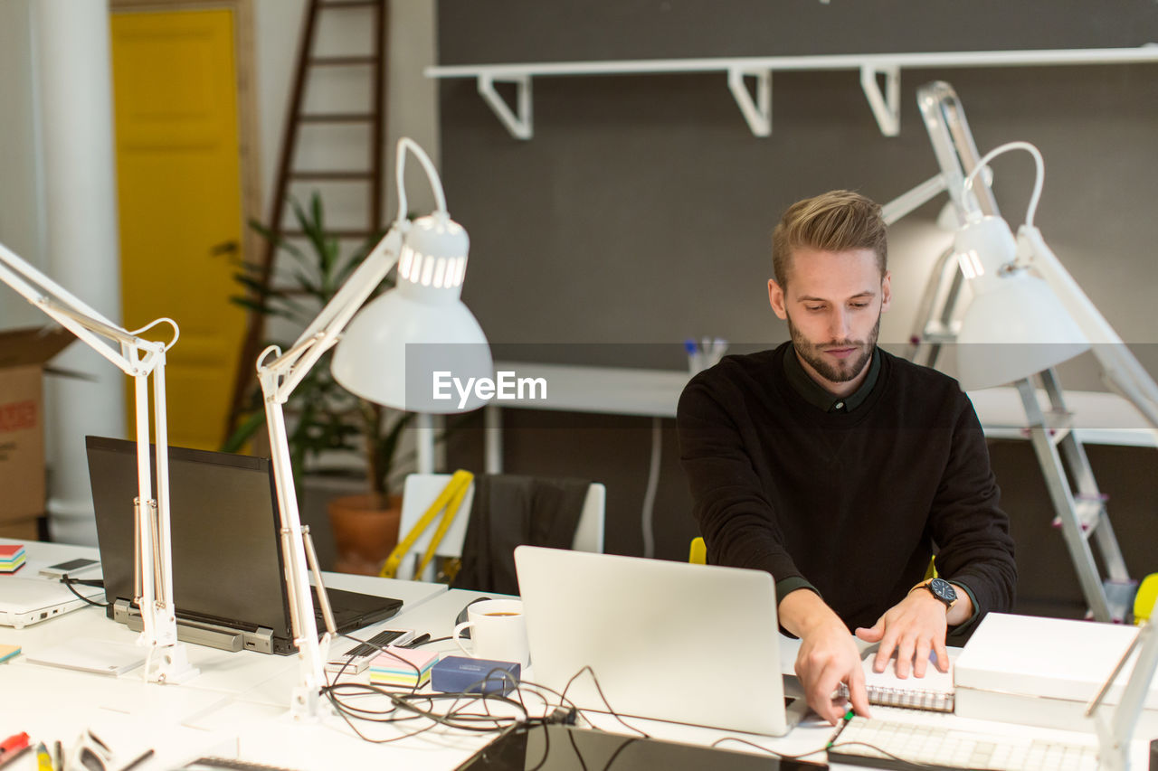 Confident young male professional working at illuminated desk in creative office