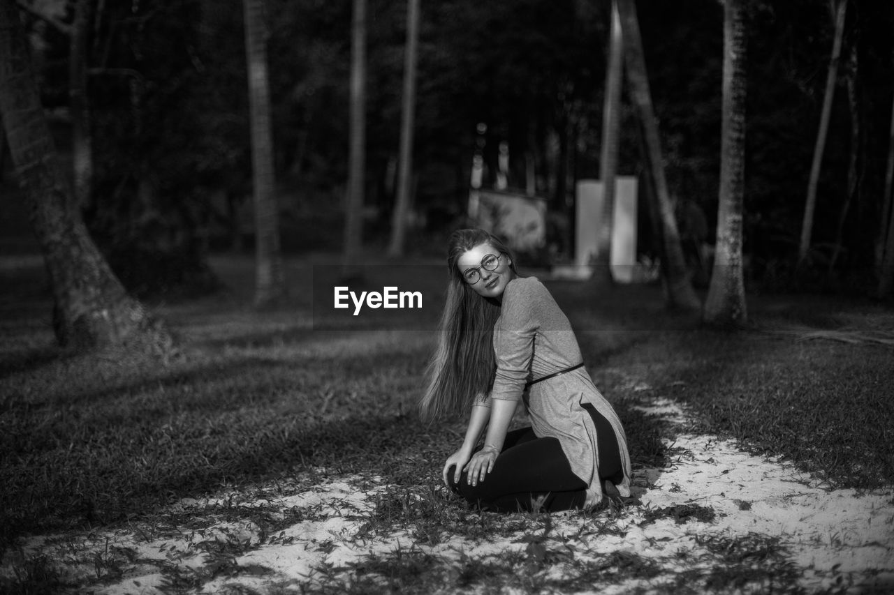 Portrait of beautiful woman kneeling against trees