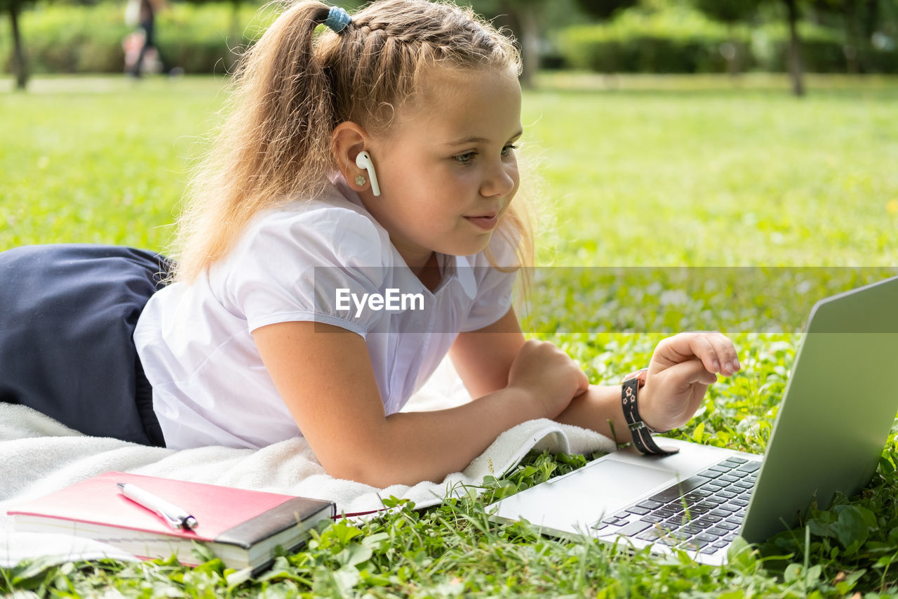 side view of young woman using laptop while sitting on field