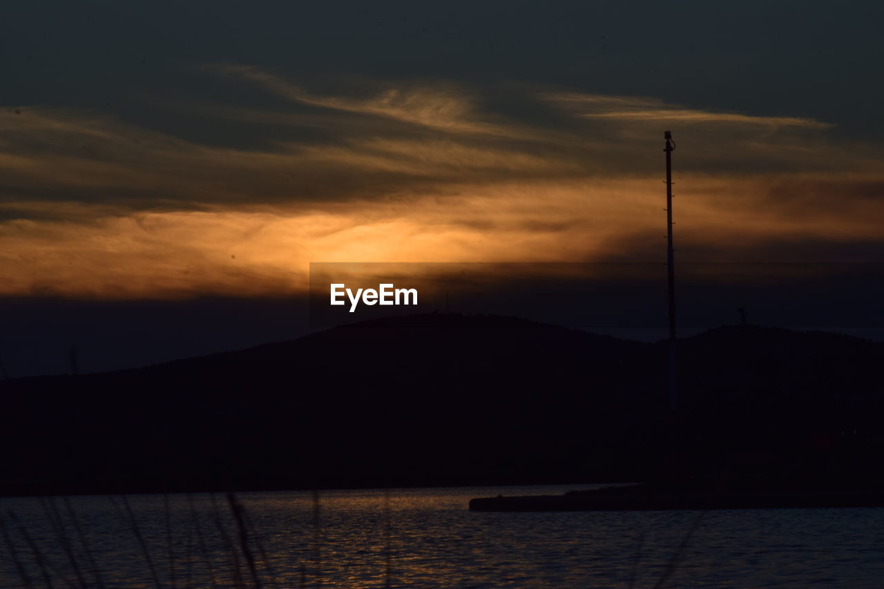 SILHOUETTE MOUNTAIN BY LAKE AGAINST ORANGE SKY