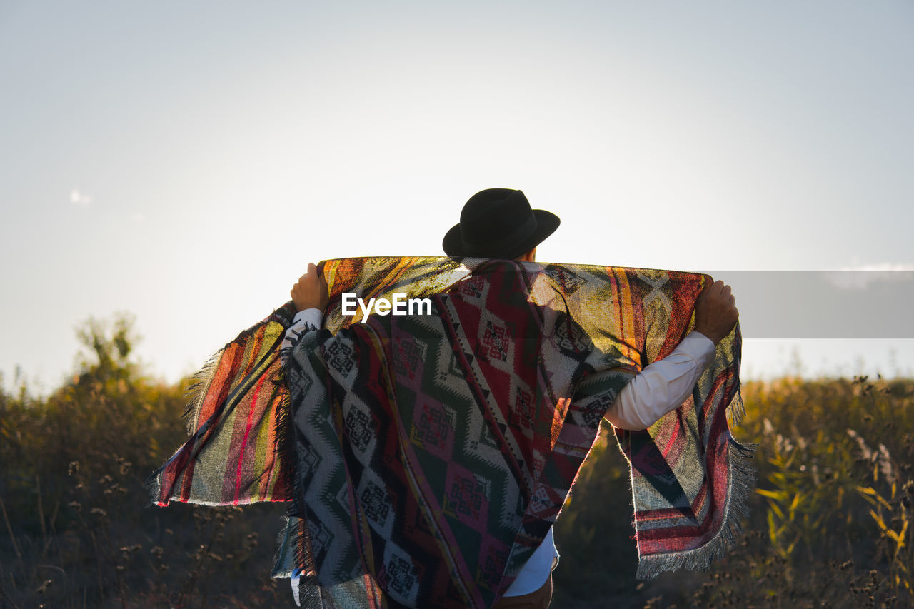 Man standing in a field poses with vintage poncho against the sun