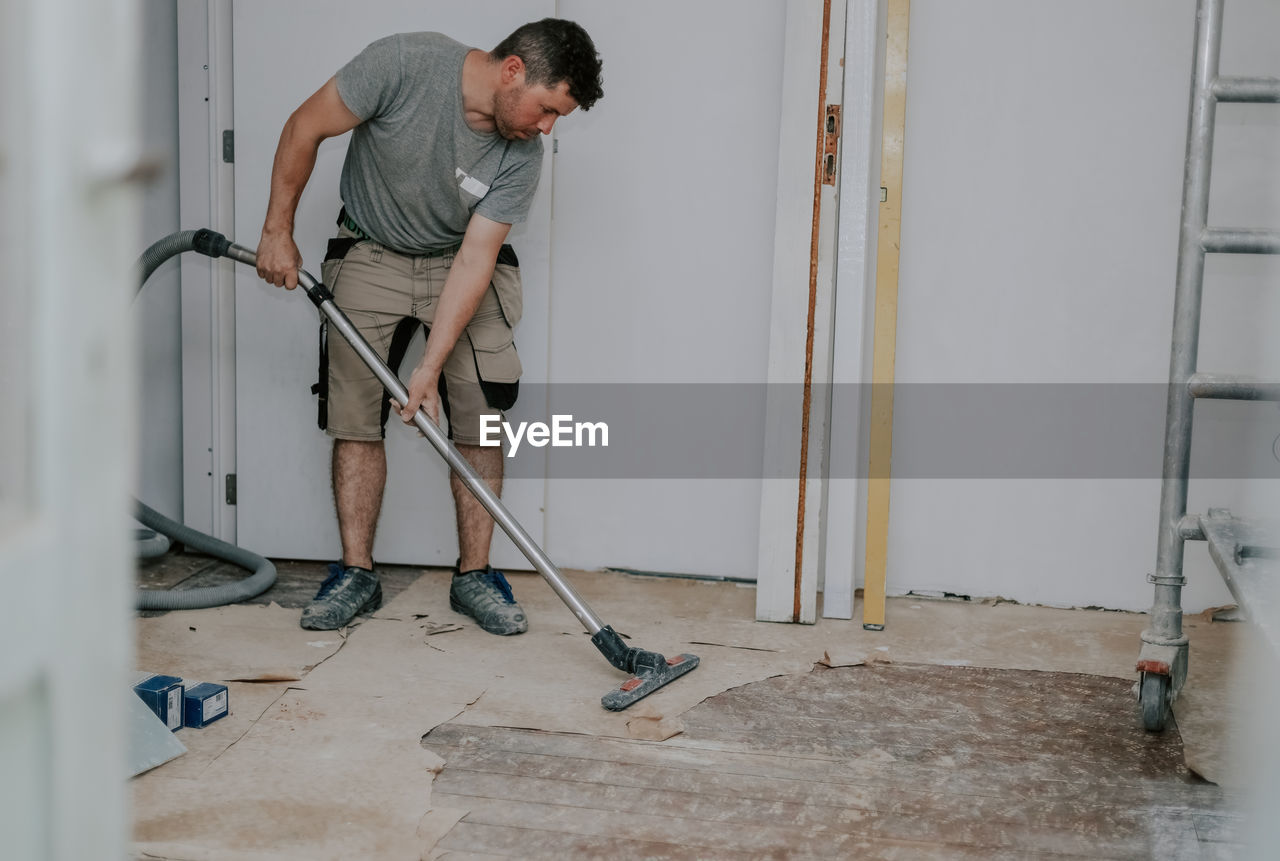 A young man vacuums the floor with a construction vacuum cleaner.