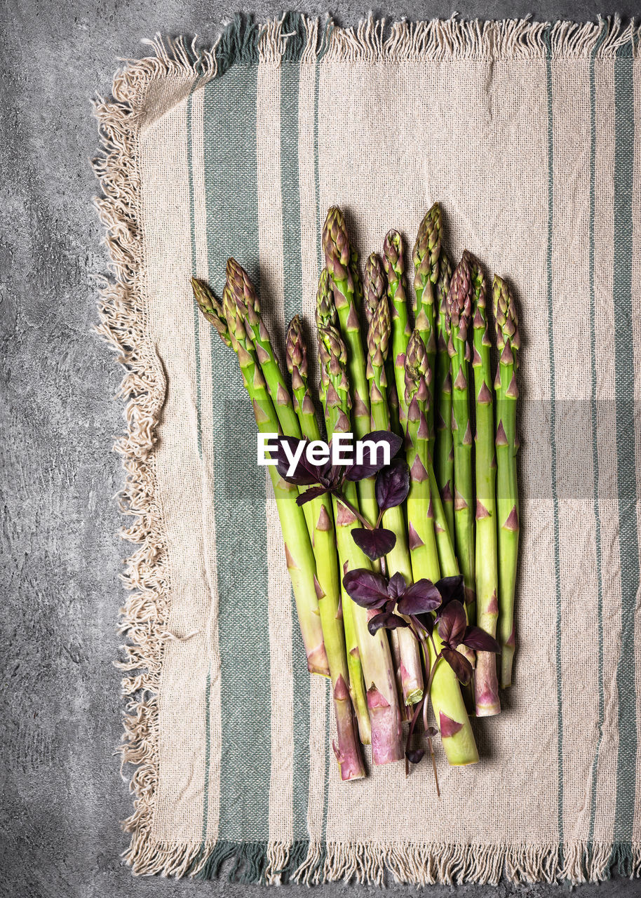 Top view of bundle of fresh green asparagus with purple basil leaves on a rustic line tablecloth. 