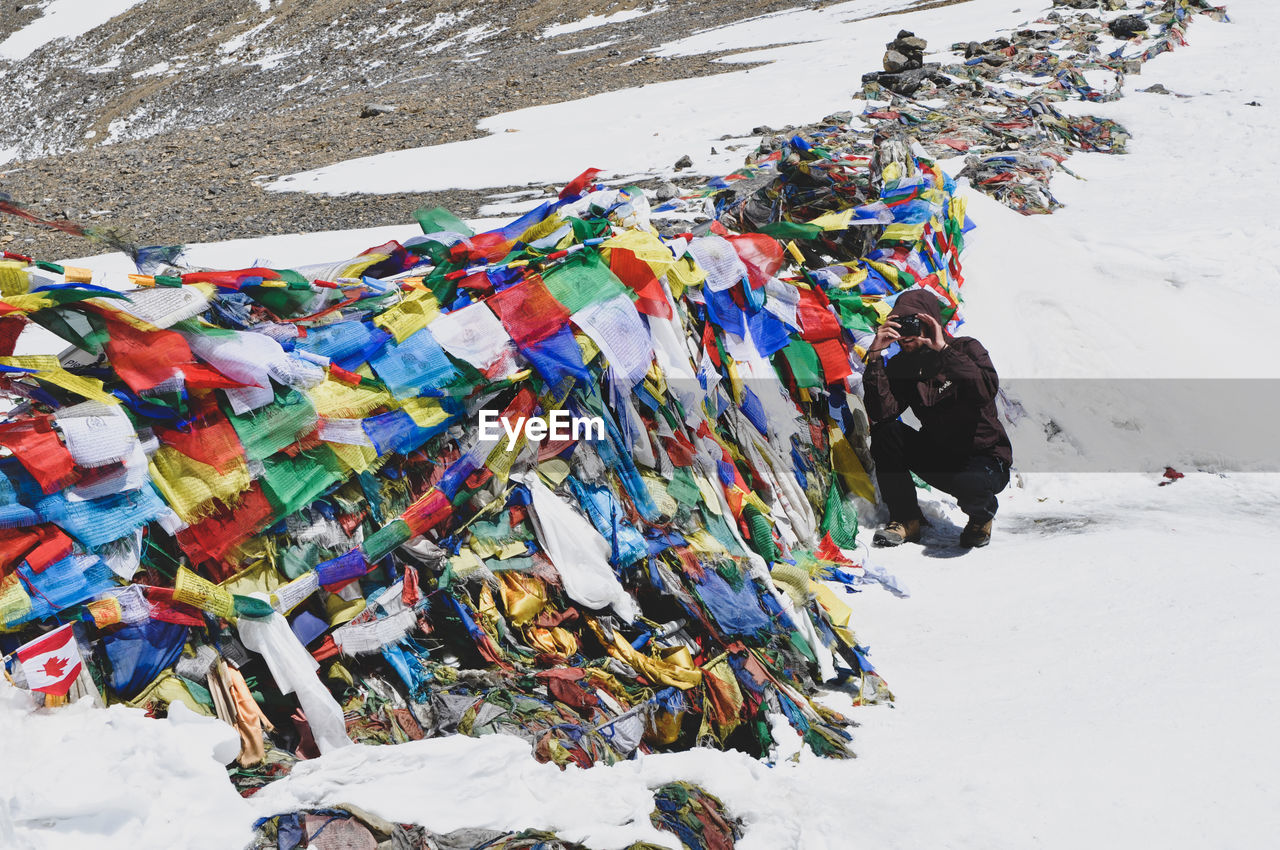 Man photographing in snow by heap of prayer flags