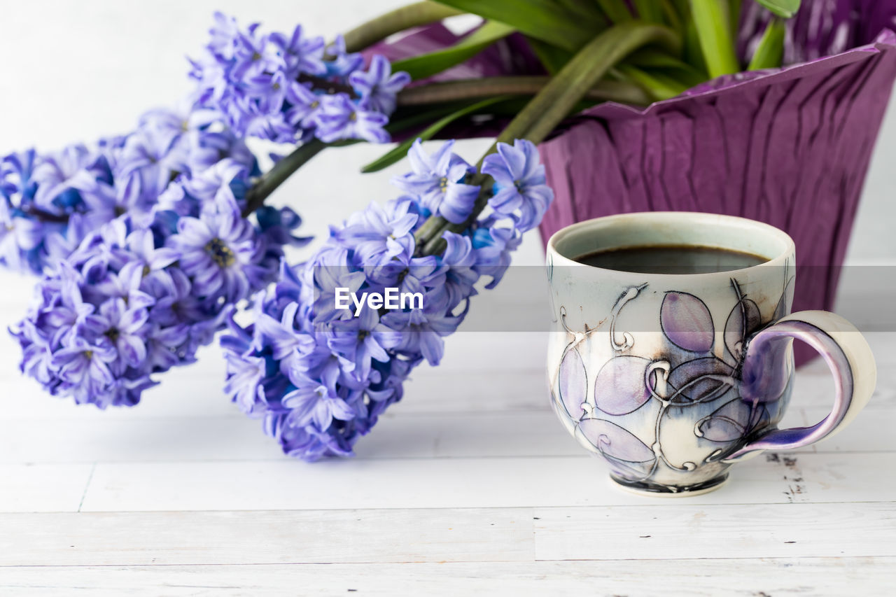 Purple hyacinth flowering plant with a cup of coffee in front.