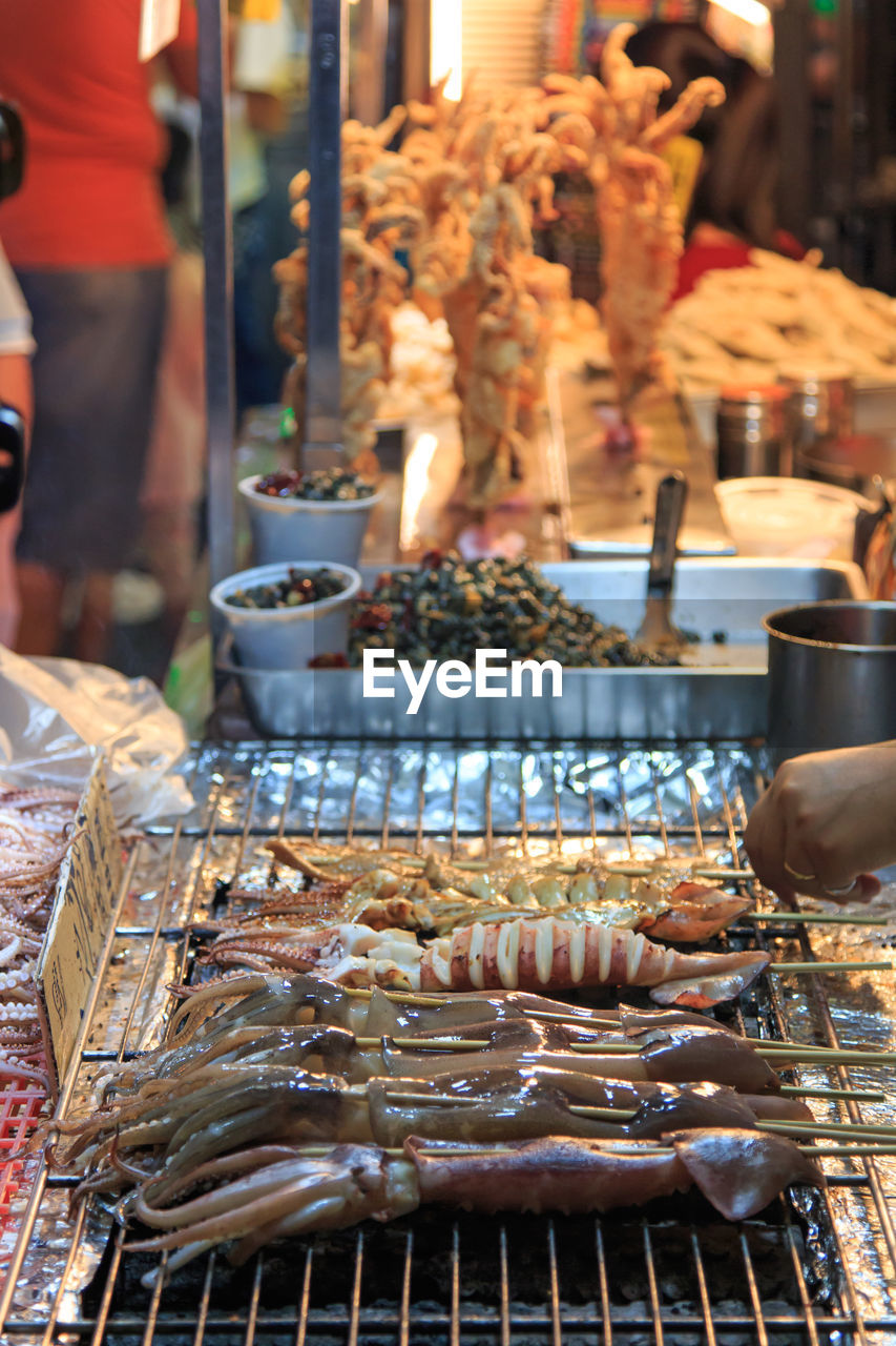 Cropped hand grilling squids on barbecue at street market