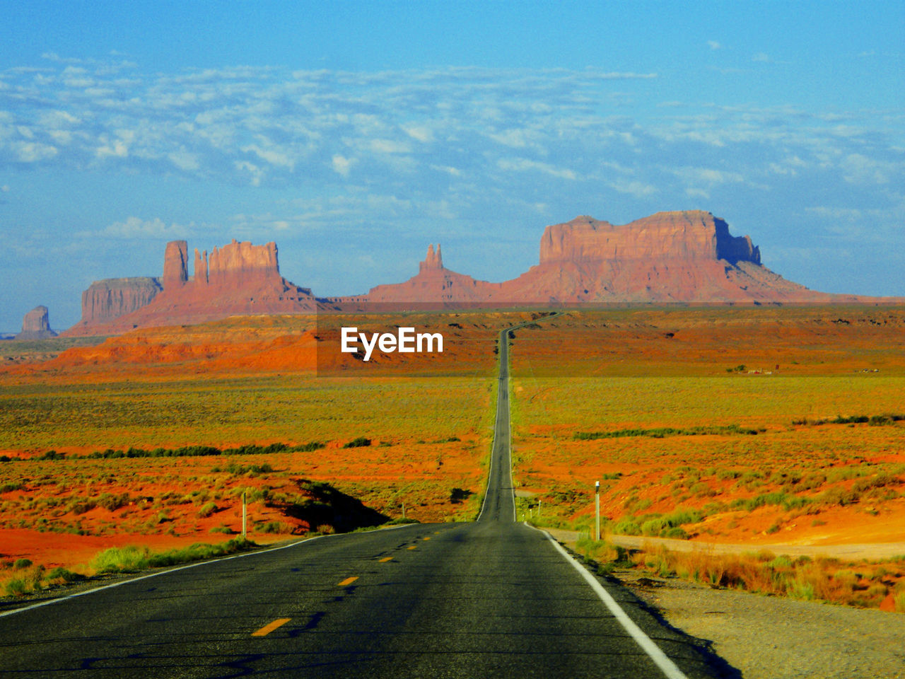 Road leading towards rocky mountains against sky at monument valley