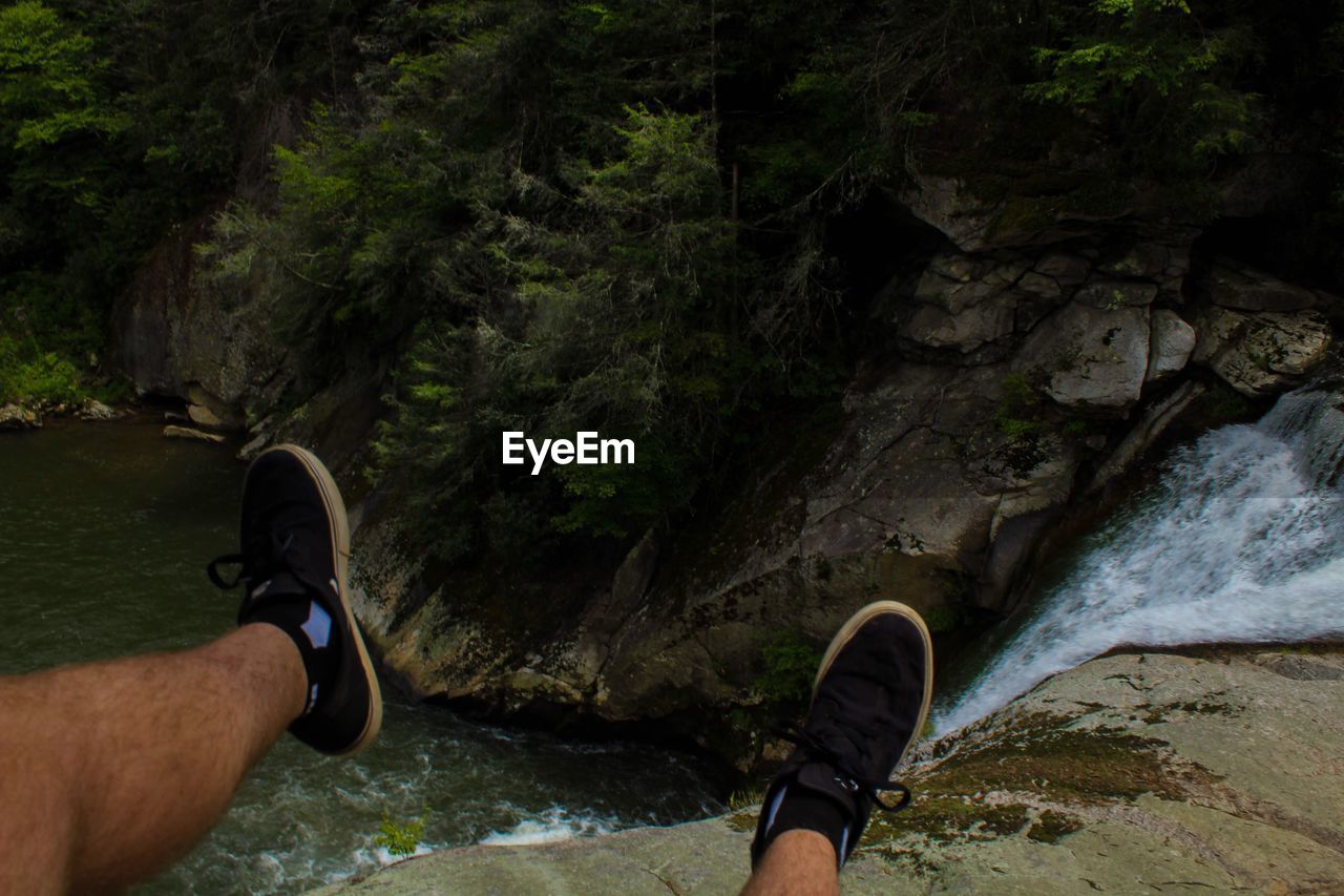 LOW SECTION OF MAN STANDING ON ROCK BY RIVER