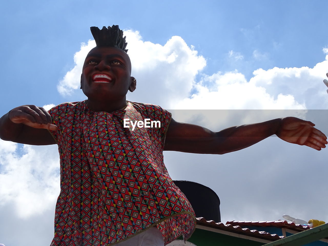 LOW ANGLE VIEW PORTRAIT OF SMILING MAN WITH ARMS RAISED AGAINST SKY