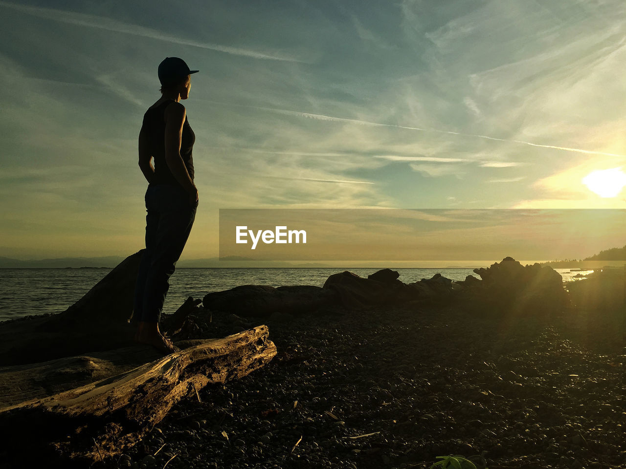 MAN STANDING ON ROCK BY SEA AGAINST SKY