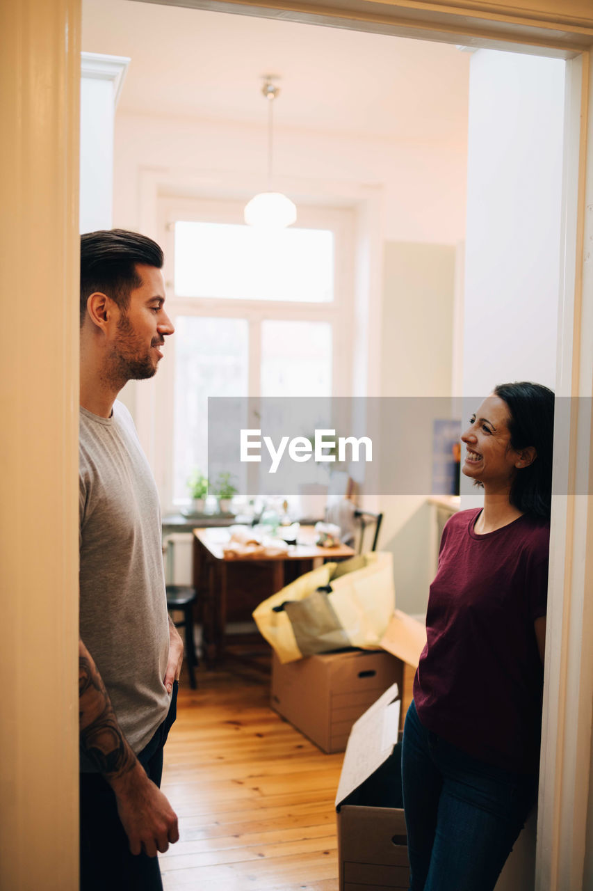 Smiling couple talking while standing at doorway in new home
