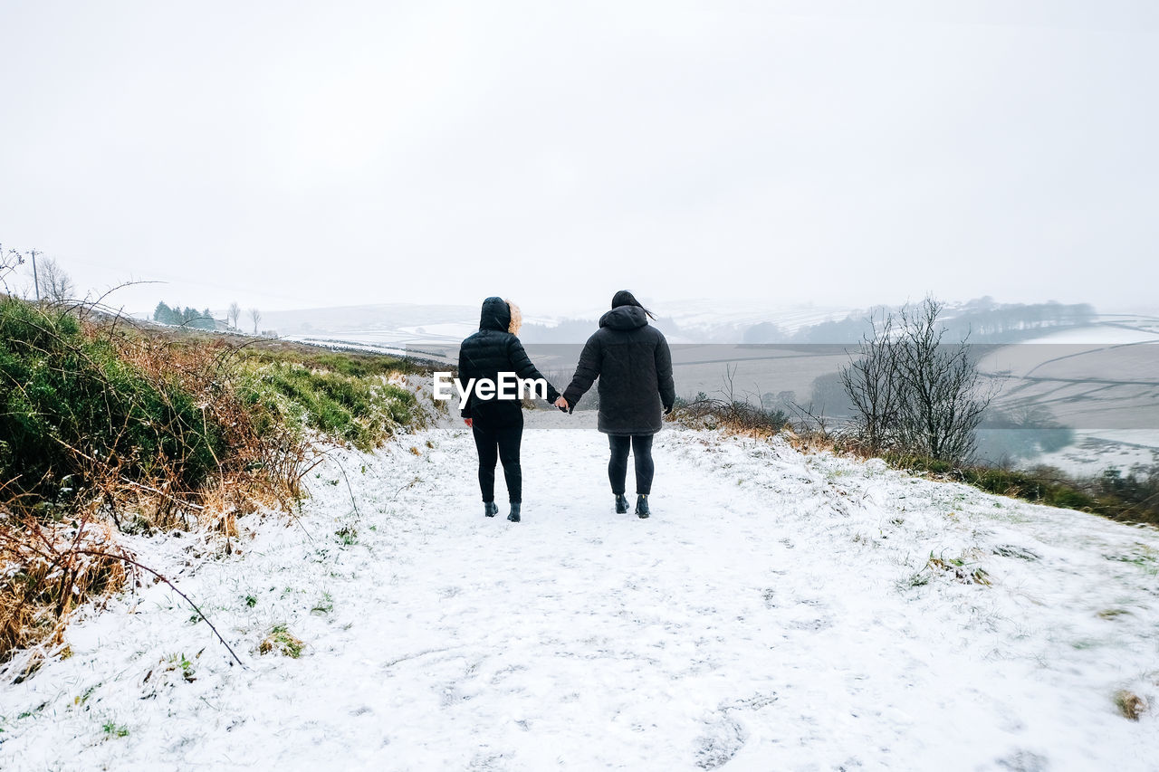 Rear view of women walking on snow covered landscape