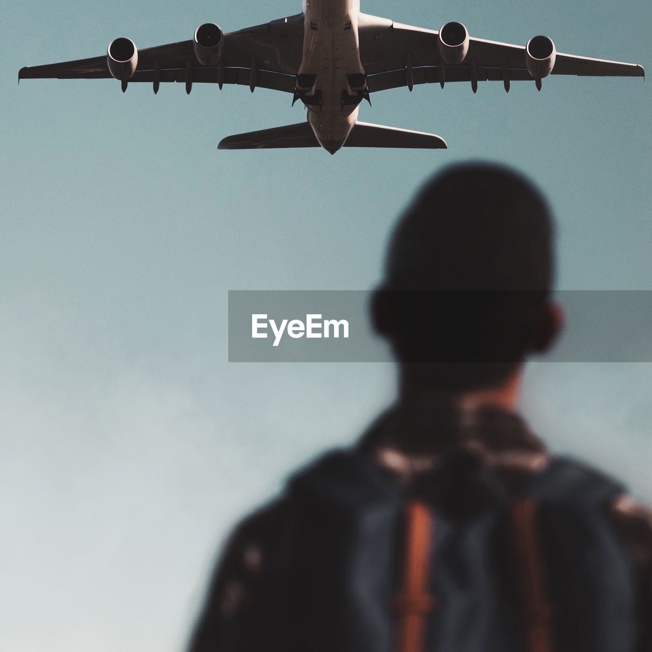 Rear view of man looking at airplane flying at sky