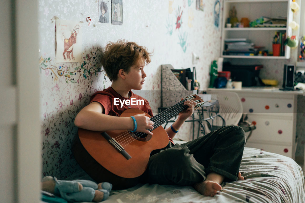 Romantic teenage redhead girl learning to play the guitar while sitting in the room.