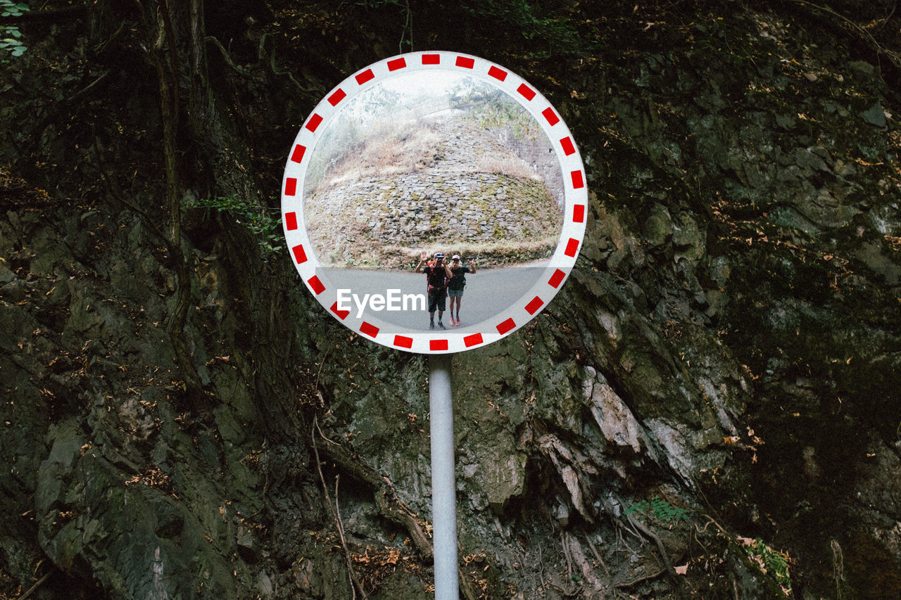 Reflection of people standing on road in road mirror against rock