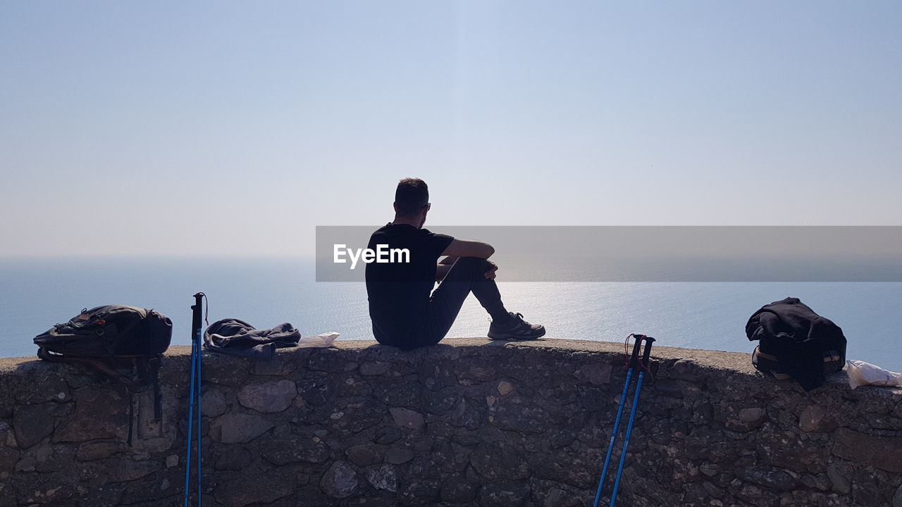 Low angle view of man walking on rock against clear sky and sea