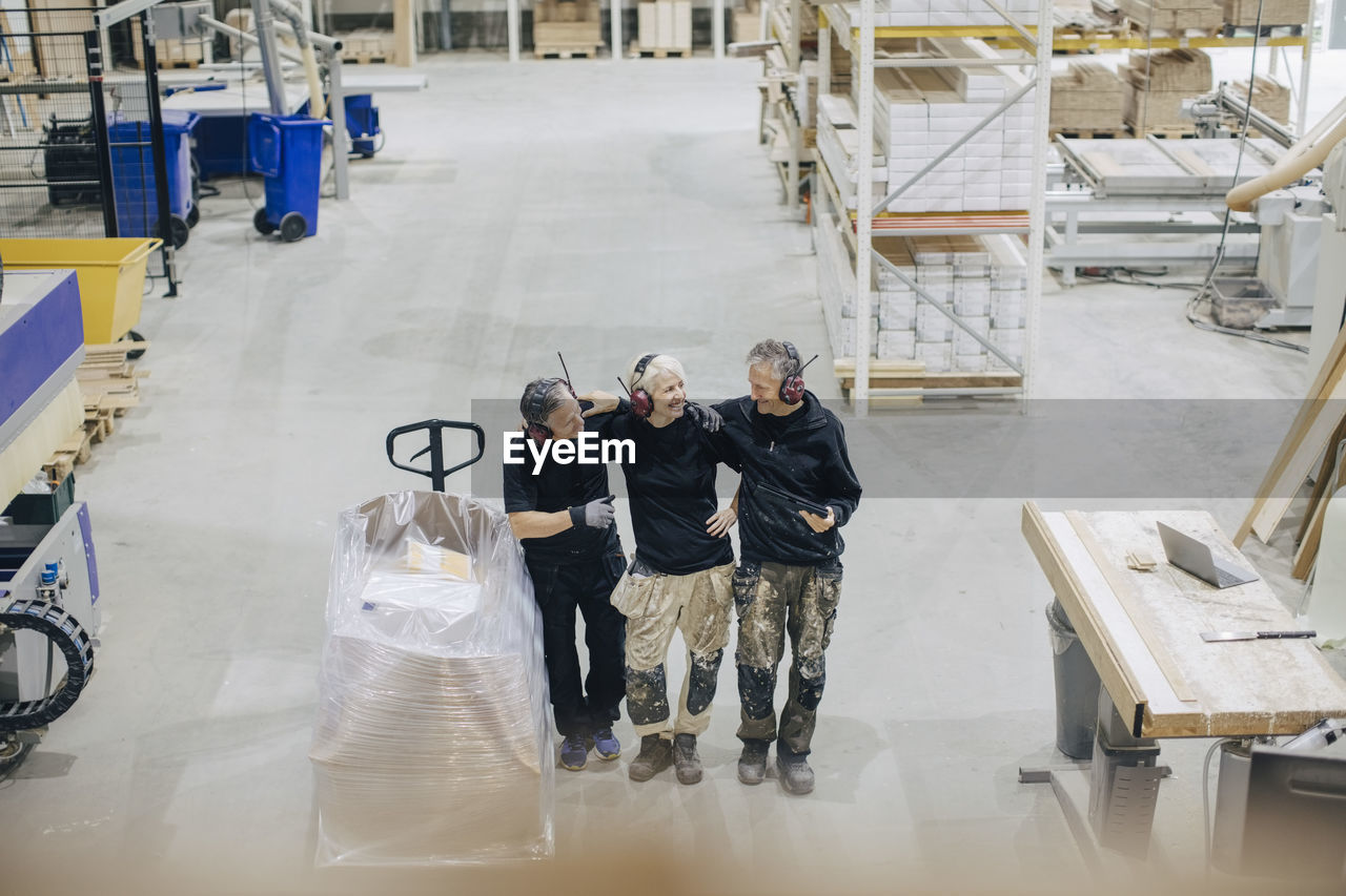 High angle view of smiling workers talking while standing by pallet jack in industry