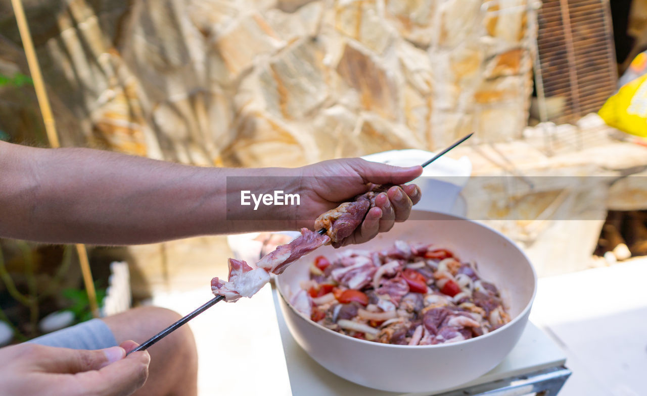 Hands of a man putting meat on skewer for barbecue. close-up image of uncooked meat on skewer.