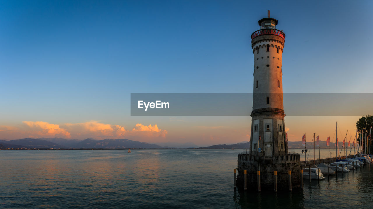 Lighthouse by sea against sky during sunset