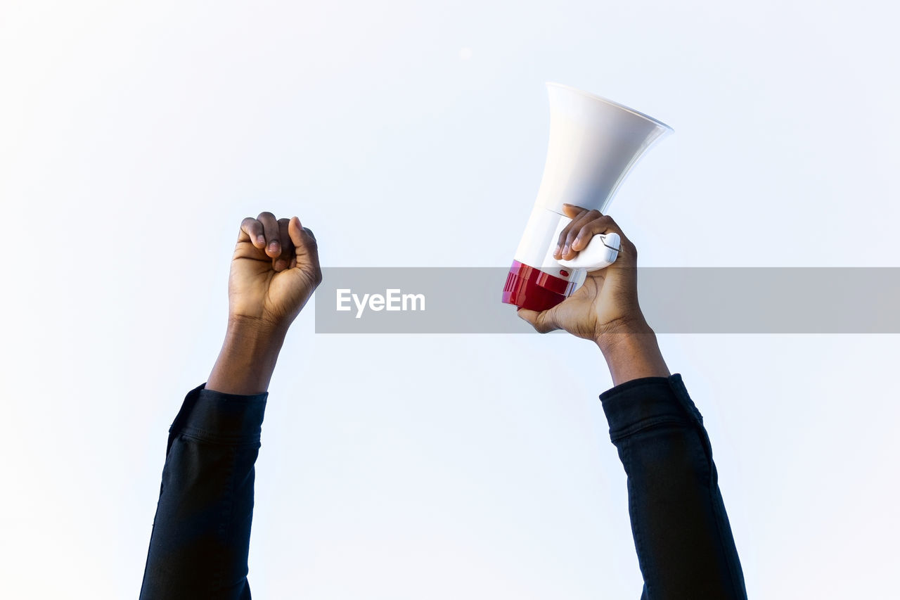 Unrecognizable crop african american male with red and white megaphone standing with fist up on white background