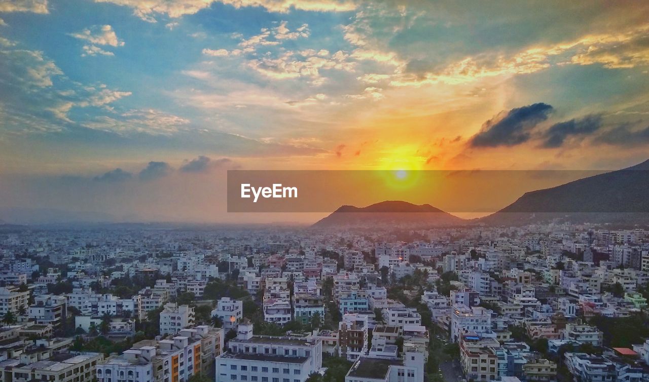 Cityscape by sea against sky during sunset