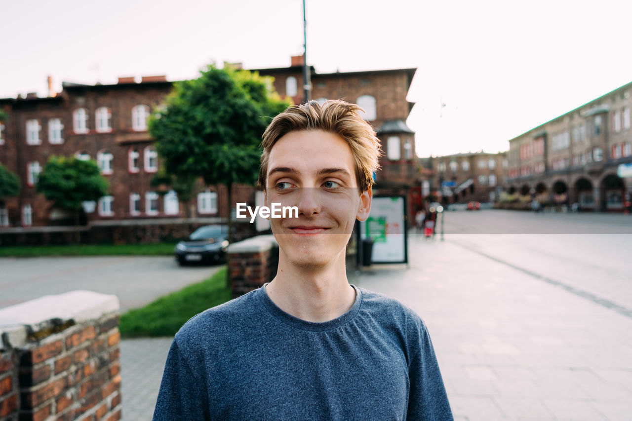 Smiling man looking away while standing on road in city