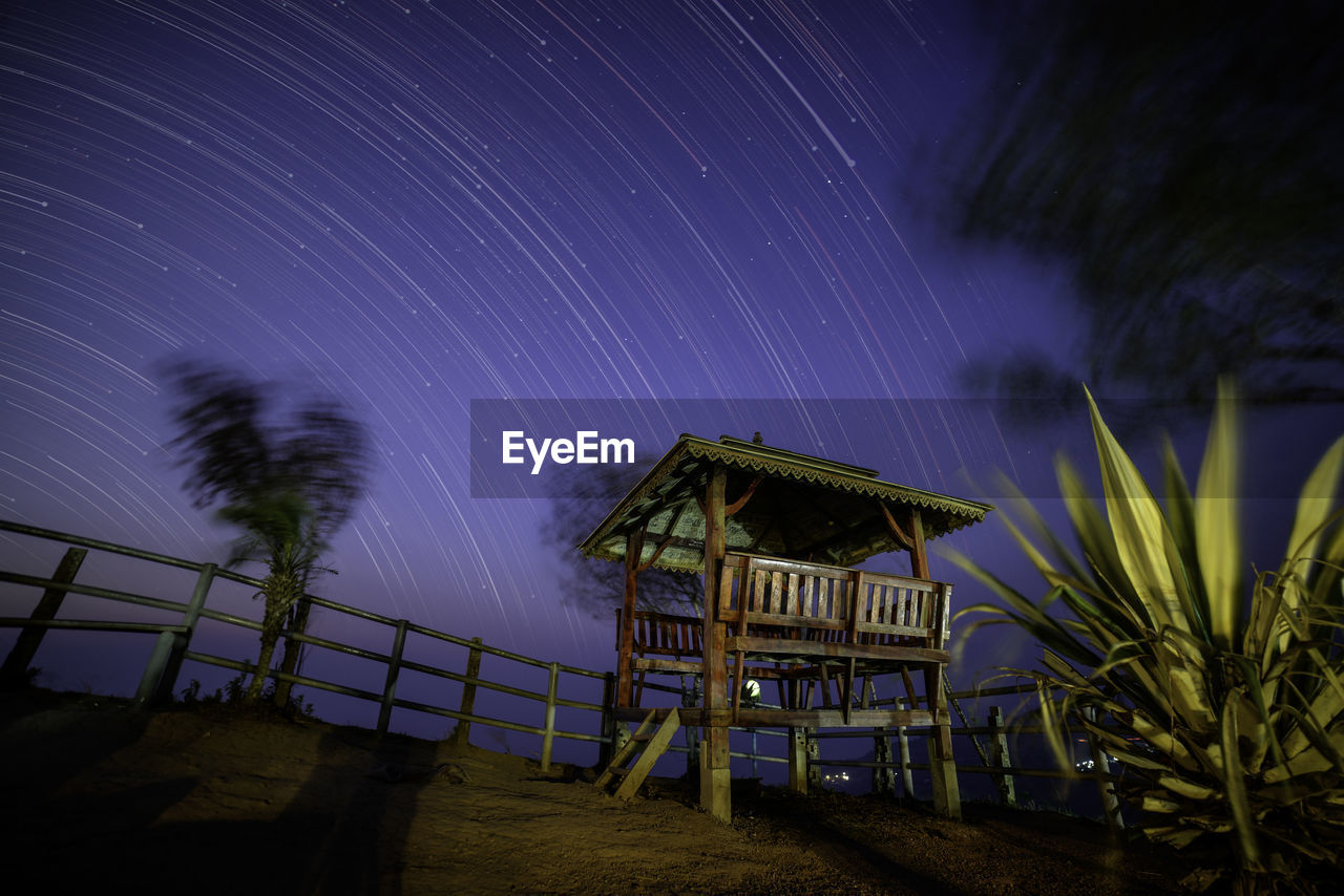 Low angle view of gazebo on field against star trails