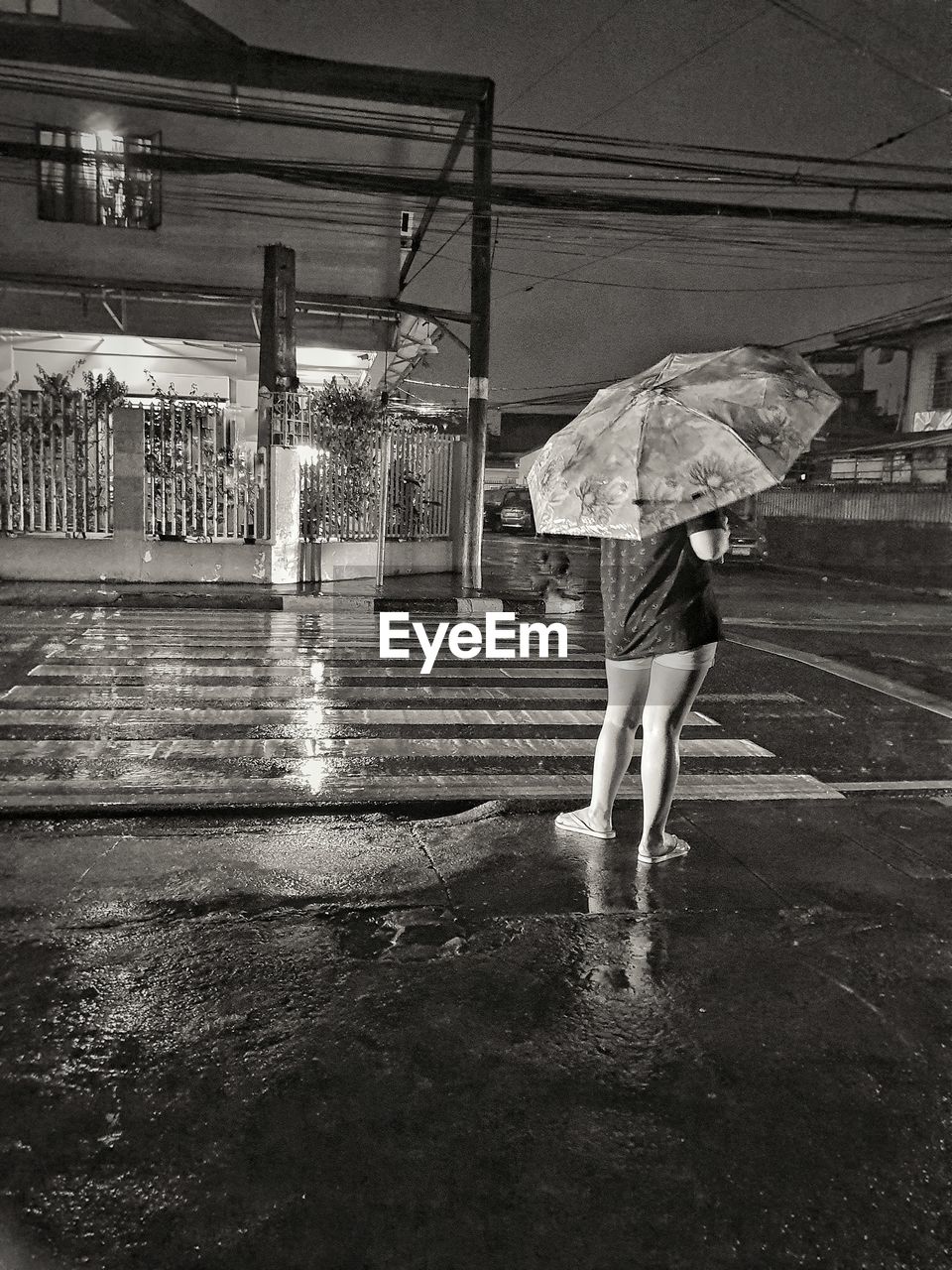 Rear view of woman with umbrella standing on wet road at night