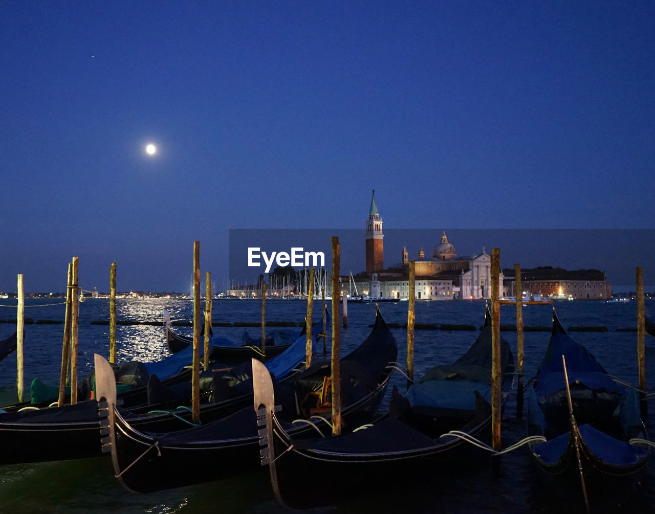 Gondolas moored along the canal with a view of st marks square all lit by a full moon. venice, italy