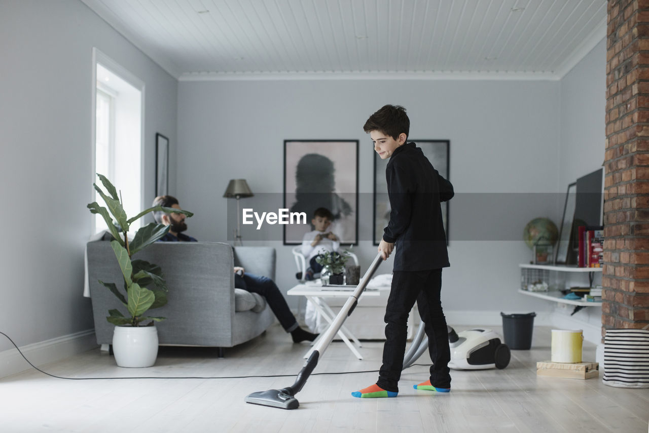 Boy vacuuming floor in living room at home