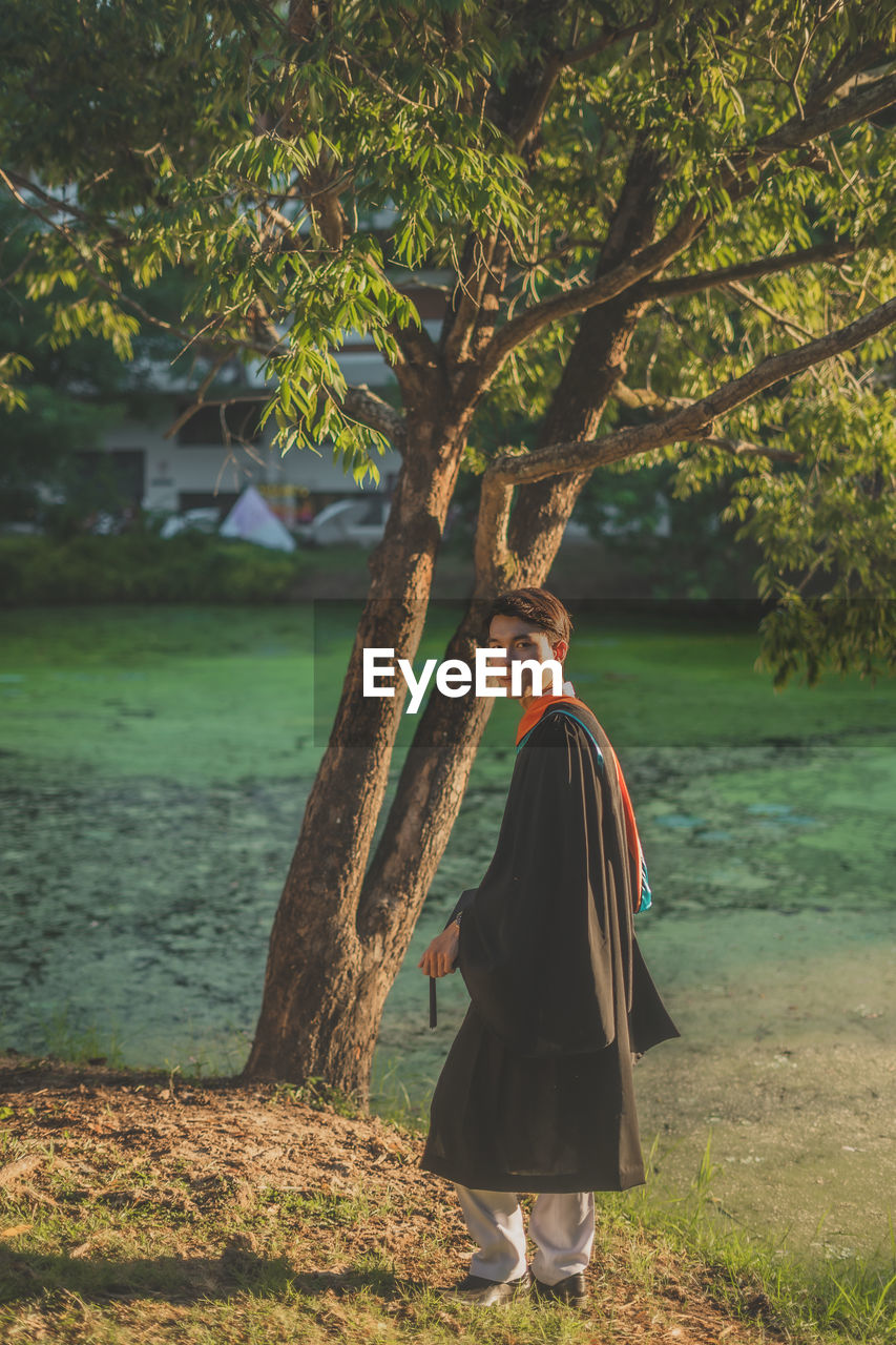 SIDE VIEW OF WOMAN STANDING BY TREE