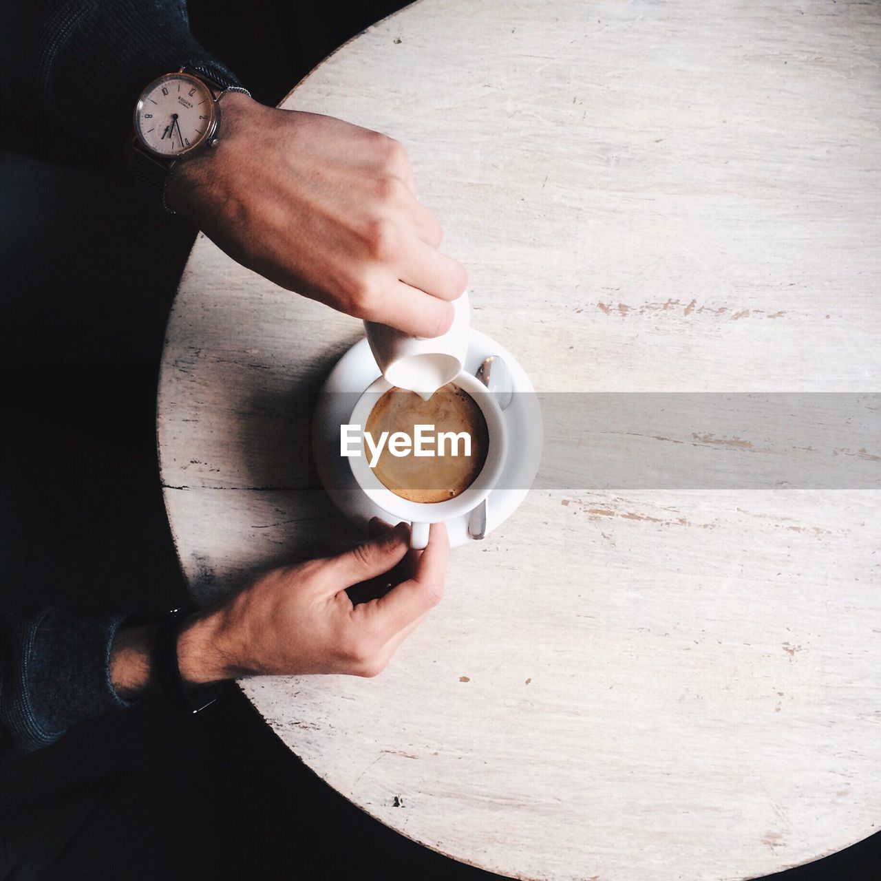 Cropped hands of man pouring milk in coffee on table