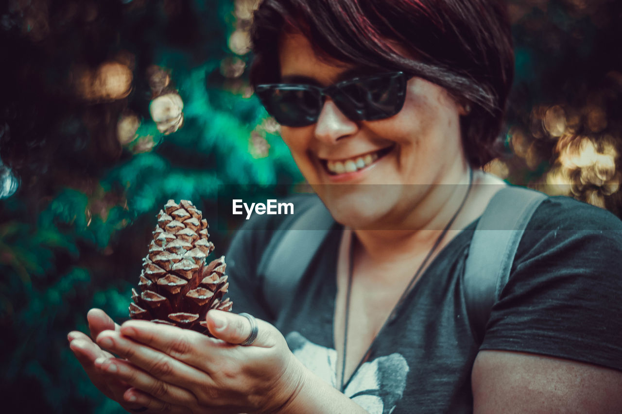 Close-up of smiling woman wearing sunglasses holding pine cone