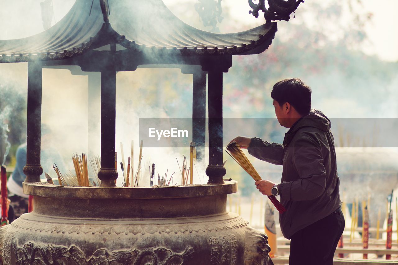 Man holding incense while standing against temple