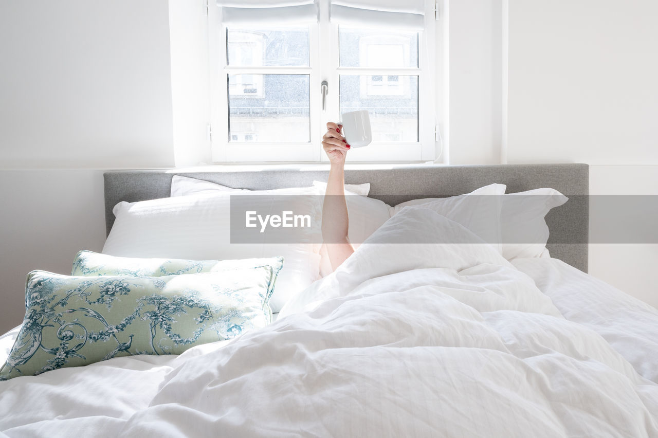 Low section of woman sleeping on bed at home - coffee cup in the air