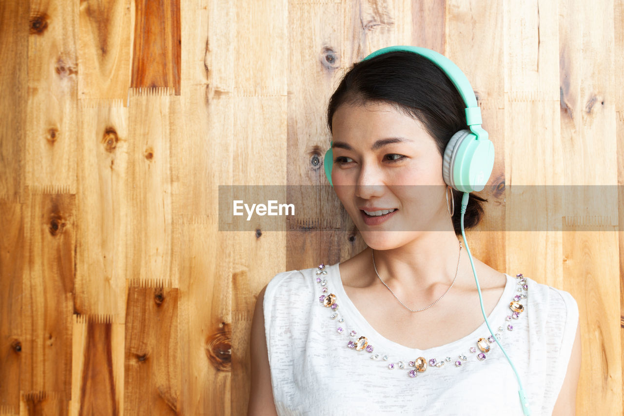 Woman listening to music against wooden wall