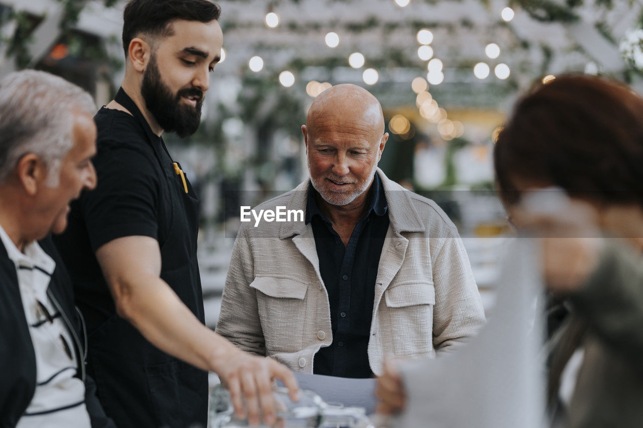 Male waiter serving water to senior man at restaurant