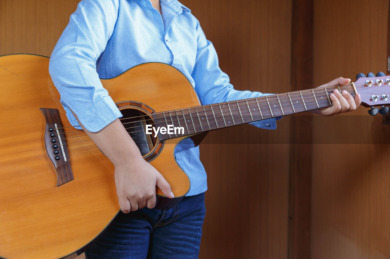 MIDSECTION OF MAN PLAYING GUITAR AT CAMERA