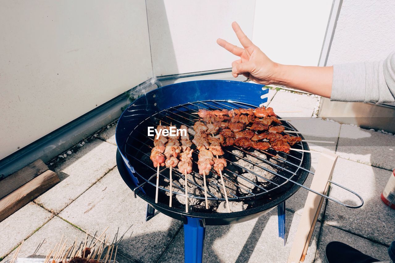 Cropped hand gesturing peace sign over meat on barbecue grill
