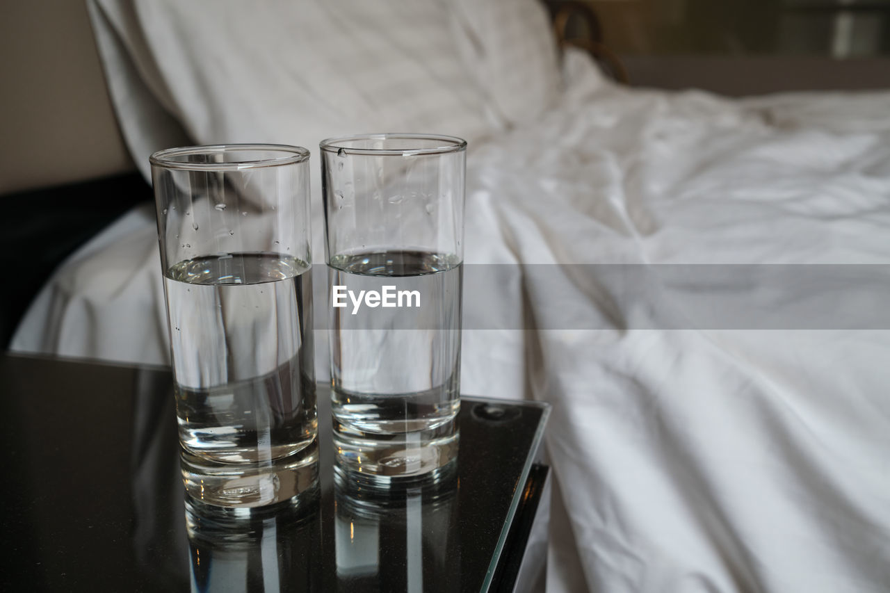 Two glass of water on the table beside the bed in the hotel room