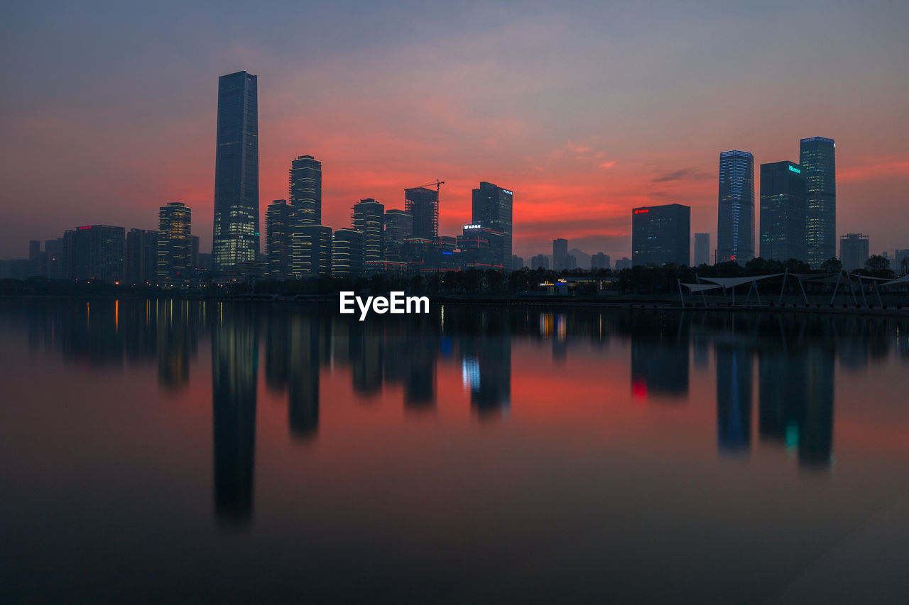 Reflection of buildings in city against sky during sunset