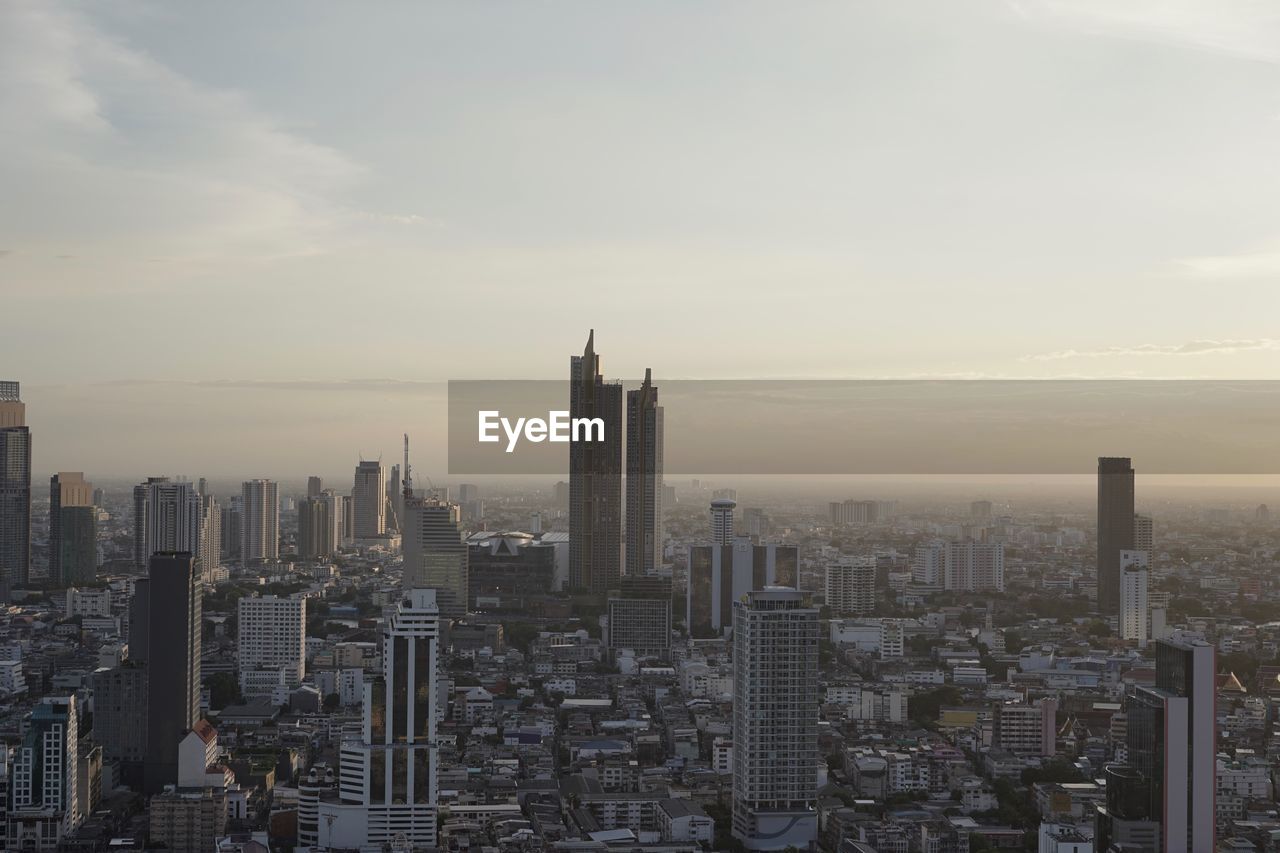 Aerial view of buildings in city against cloudy sky