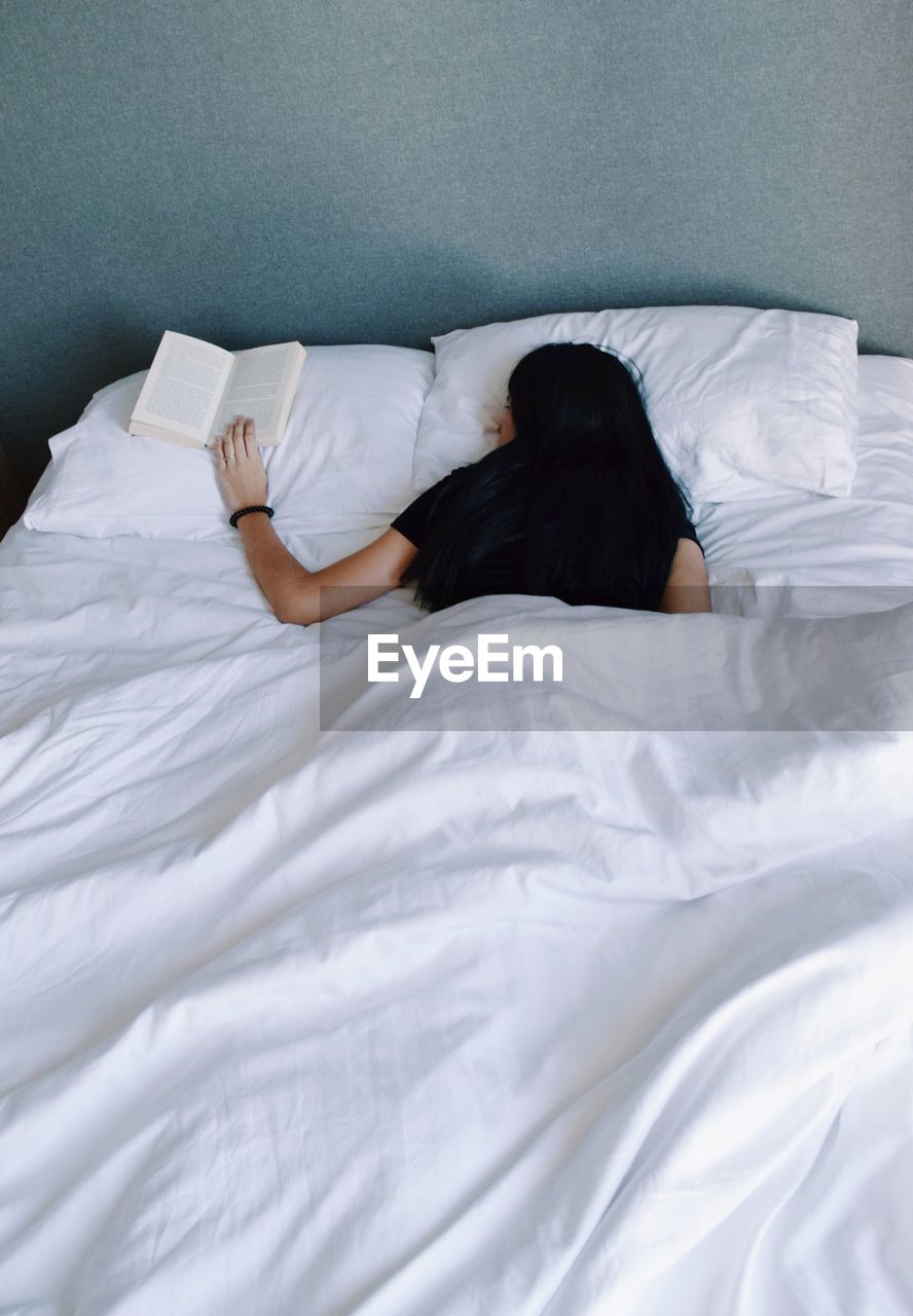 Woman holding book while sleeping on bed at home