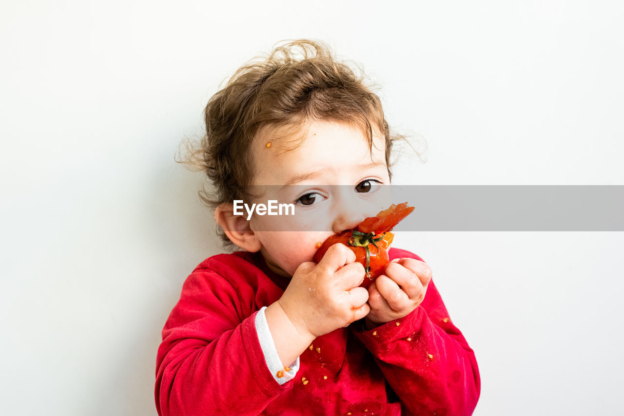 Portrait of cute boy eating strawberry against white background