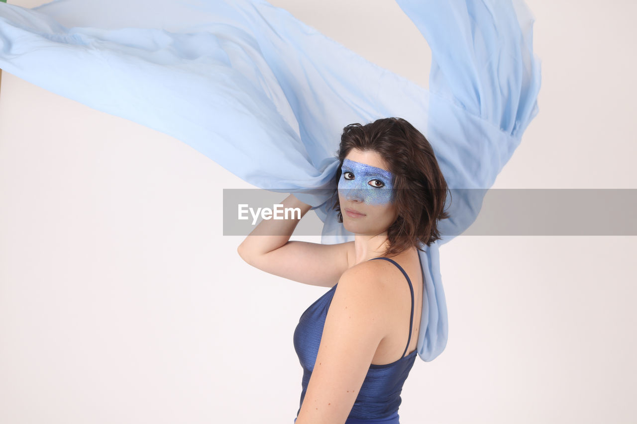 Side view portrait of female model with blue face paint against white background