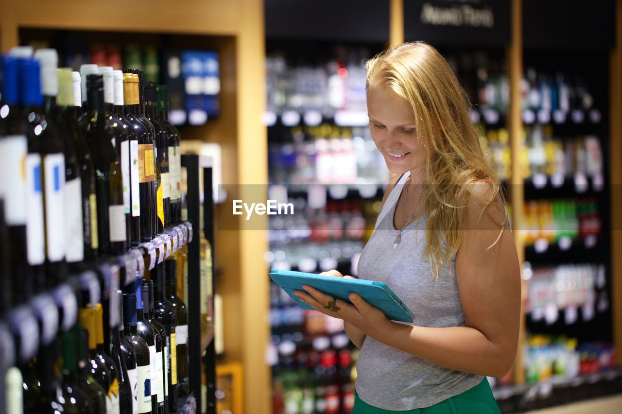 Woman using digital tablet while standing at wine store