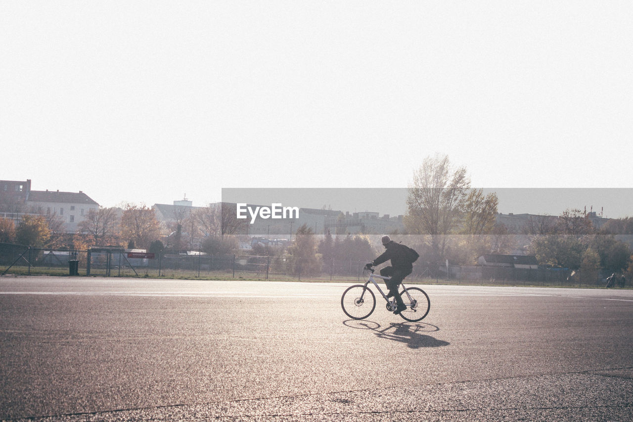 Man riding bicycle on street against clear sky during sunny day