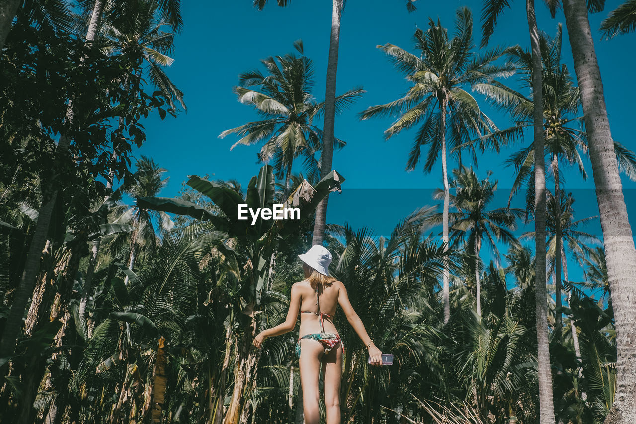 Woman in bikini standing against palm trees