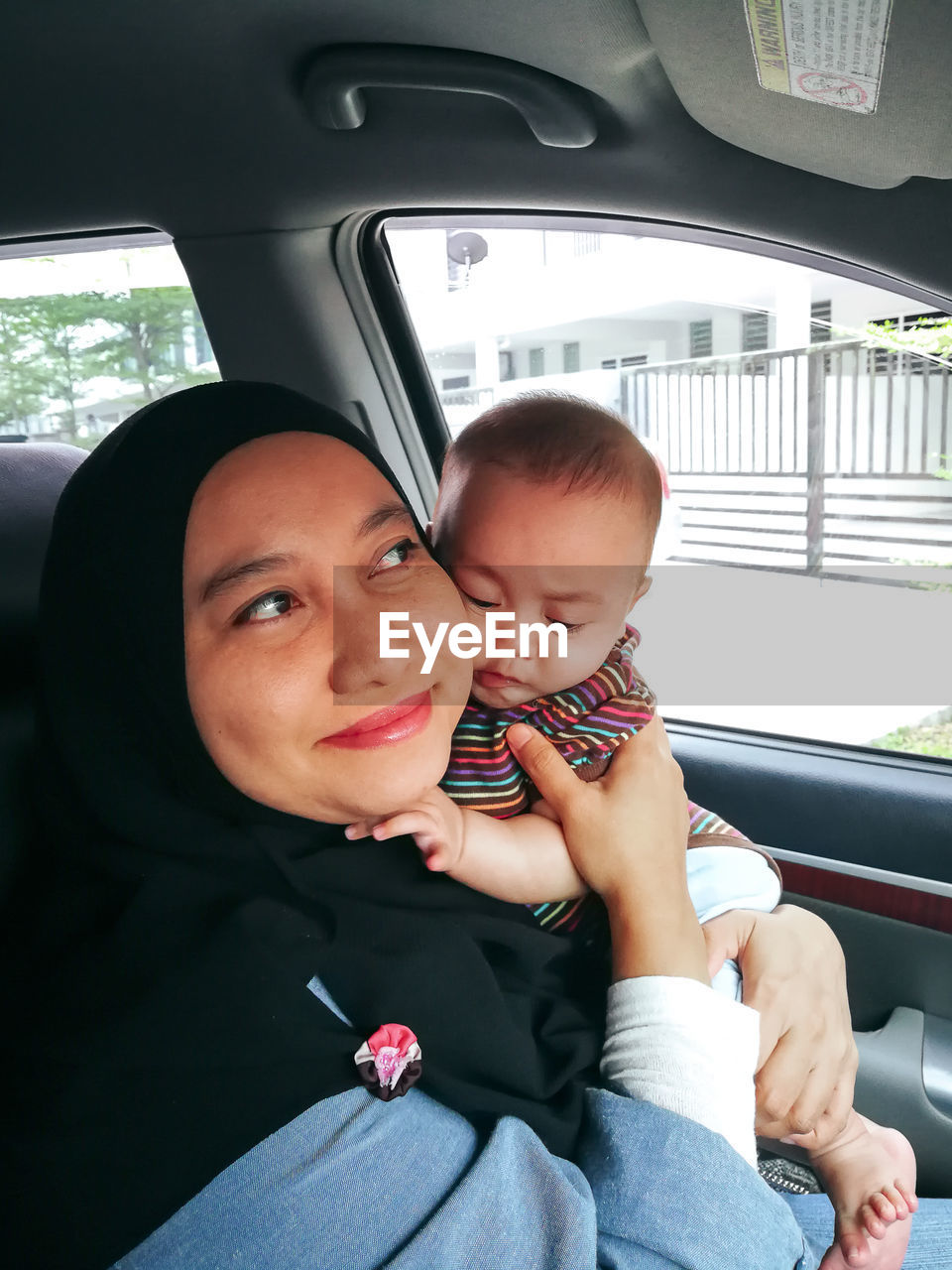 Muslim mother holding little baby daughter. asian wearing head scarf, sitting in the car with baby.